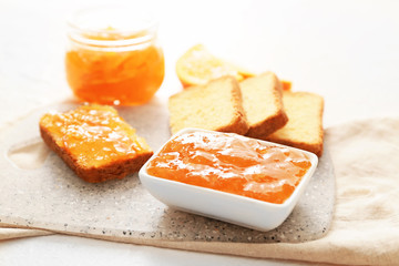 Fototapeta na wymiar Bowl of orange jam with slices of bread on table