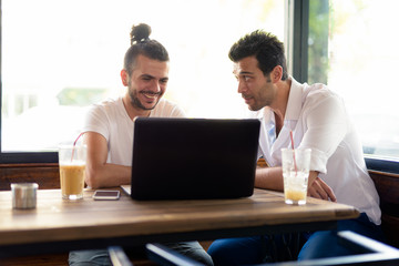 Obraz premium Two happy men as friends using laptop together at the coffee shop