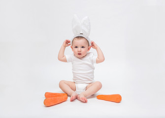 baby boy on a white background in a white bodysuit. A small boy with Bunny ears and a carrot
