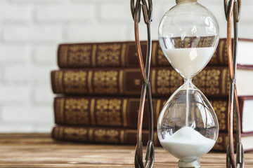 Vintage hourglass against a stack of old books close up