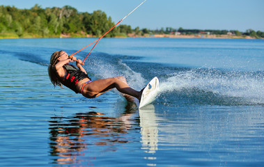 Beautiful girl wakeboarding on the shore of the river sea in the summer on a spring day in a jacket - obrazy, fototapety, plakaty