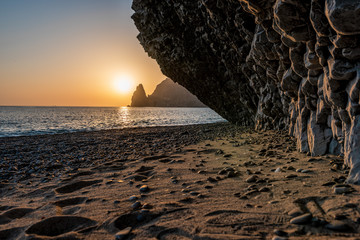 view of the sunset sea and the beach, the rock volcanic rock is lit by the warm sunset, sand and...