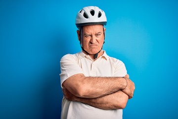 Middle age hoary cyclist man wearing bike security helmet over isolated blue background skeptic and nervous, disapproving expression on face with crossed arms. Negative person.
