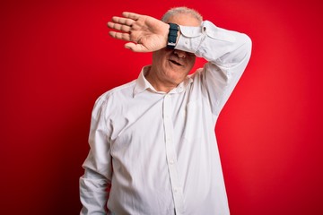 Naklejka premium Middle age handsome hoary man wearing casual shirt and glasses over red background covering eyes with arm smiling cheerful and funny. Blind concept.