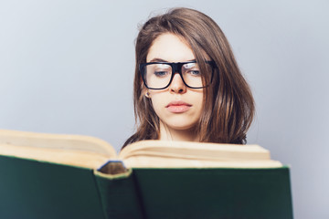 girl with glasses reading a book, looking from her