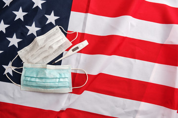 Used protective masks and digital thermometer on american flag background. Covid-19 quarantine. Flat lay, top view, copy space