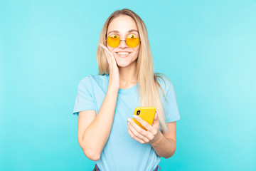 Portrait of a surprised young beautiful woman posing isolated over blue wall background playing games by mobile phone.