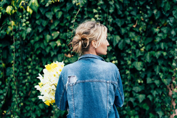 g charming blonde hipster in a denim jacket with a bouquet of daffodils