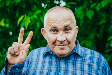 Aged boomer man making OK peace sign over green park background. Winner. Success. Positive senior smiles to camera.