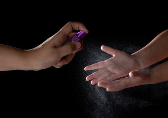Using alcohol spray antivirus sanitizer on child's hands on black background