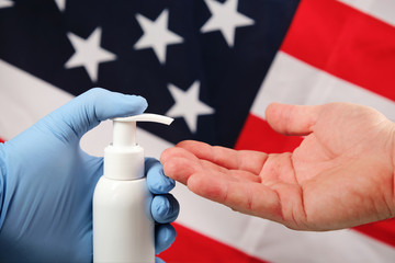 Doctors hand in blue medical glove applying antiseptic alcohol gel on hand without a glove to prevent infections coronaviruses, bacteria and germs, on american flag background