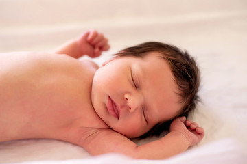 Fototapeta na wymiar Little infant child sleeping on light beige blanket with arms raised to head. Beatuful and carefree little newborn baby laying on back with closed eyes. Safe and hapyy childhood concept