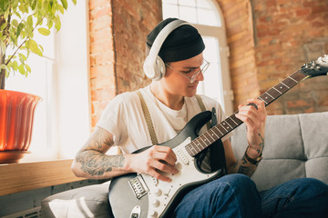 Obraz premium Man studying at home during online courses or free information by hisself. Becomes musician, guitarist while isolated, quarantine against coronavirus spreading. Using laptop, smartphone, headphones.