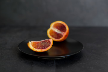 A slice of juicy ripe red bloody orange on a black plate against a black background.