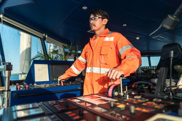 Filipino deck Officer on bridge of vessel or ship wearing coverall during navigaton watch at sea . He is maneuvering with cpp thrusters propulsion