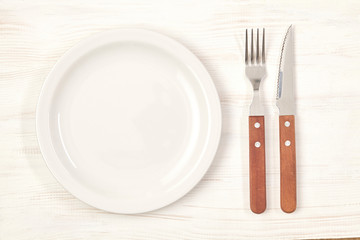 Ceramic plate with fork and knife on wooden table. Top view.