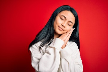 Young beautiful chinese sporty woman wearing sweatshirt over isolated red background sleeping tired dreaming and posing with hands together while smiling with closed eyes.