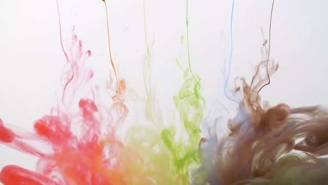 Multicolored rainbow paint drops from above mixing in water, colored smoke clouds spreading underwater on white background, colorful background