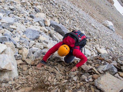 a man scrambling up a steep mountain slope covered with scree