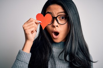 Young beautiful chinese woman holding paper heart over isolated white background scared in shock with a surprise face, afraid and excited with fear expression