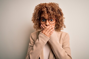 Beautiful african american businesswoman wearing glasses over isolated white background shocked covering mouth with hands for mistake. Secret concept.