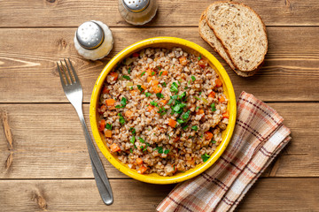 Buckwheat porridge with vegetables and mushrooms in ceramic bowl on rustic wooden table