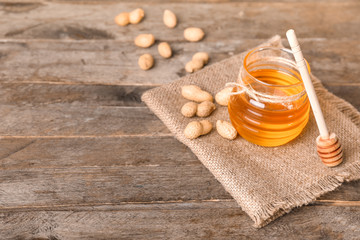 Jar of sweet honey and peanuts on wooden background