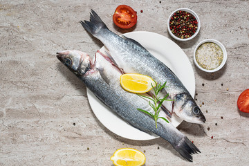 Raw wild sea bass ready to cook with spices, lemon and rosemary on light marble table top view. Healthy food concept.