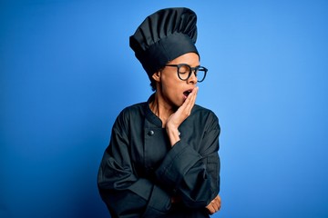Young african american chef woman wearing cooker uniform and hat over blue background bored yawning tired covering mouth with hand. Restless and sleepiness.
