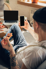 Scrolling news. Man studying at home during online courses, smart school. Getting classes or profession while isolated, quarantine against coronavirus spreading. Using laptop, smartphone, headphones.