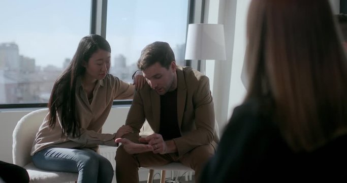 Sympathetic young asian woman pities a sad young caucasian male gamer at meetings of anonymous gamers. Concept of getting rid of addiction and help from sympathetic people