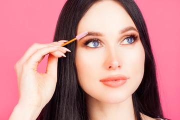Women's eyebrows, portrait of a woman in close-up, she combs her brow with a special brush, on a pink background. The concept of eyebrow shaping or eyebrow shape.