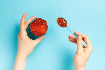 Flat lay of woman eating red caviar against blue background