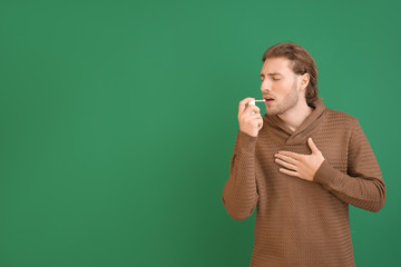 Ill young man with inhaler on color background