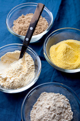 Various vegetable gluten free flour corn,sesame,oat,coconut in glass bowl on blue textile background close-up.Alternative to wheat flour for paleo diet.Healthy eating,dieting food concept