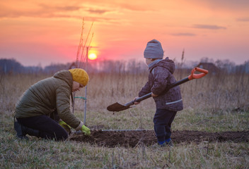 a funny little boy is digging with a shovel in the garden with his mother on a spring evening at...