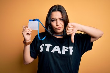 Young brunette worker woman wearing staff t-shirt as uniform showing id card with angry face,...