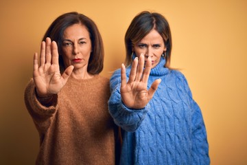 Middle age beautiful couple of sisters wearing casual sweater over isolated yellow background doing...