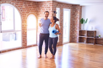 Middle age beautiful sporty couple smiling happy. Standing with smile on face hugging and holding mat at gym