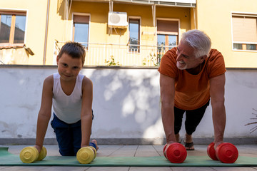 Fototapeta premium father and young son are training with colored dumbbells on a terrace