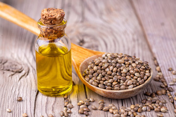 Heap of dried organic hemp seeds or cannabis plant seeds in spoon with glass of hemp seed oil on wooden backdrop. cannabis herb concept. hemp seed used birdseed