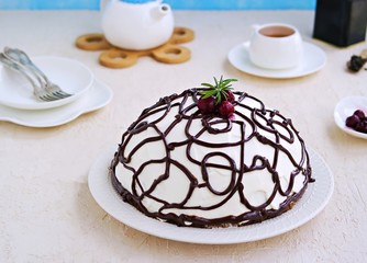 Dessert, homemade cake with chocolate biscuit, cherry and cream of sour cream and whipped cream on a white plate on a light concrete background.
