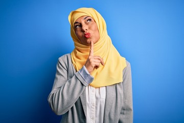 Middle age brunette business woman wearing muslim traditional hijab over blue background Thinking concentrated about doubt with finger on chin and looking up wondering