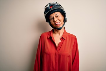 Middle age motorcyclist woman wearing motorcycle helmet over isolated white background sticking tongue out happy with funny expression. Emotion concept.