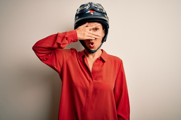 Fototapeta premium Middle age motorcyclist woman wearing motorcycle helmet over isolated white background peeking in shock covering face and eyes with hand, looking through fingers with embarrassed expression.