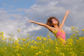 An attractíve young woman stands in a rapeseed field 
in springtime. She has a pink top on and wears trendy
pink glasses.  