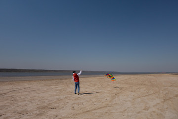 A 10 year old boy in a white sweatshirt and orange vest launches a kite on a deserted beach in solitude.