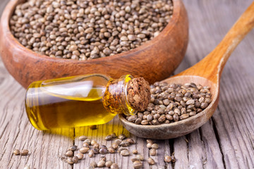 Heap of dried organic hemp seeds or cannabis plant seeds in spoon with glass of hemp seed oil on wooden backdrop. cannabis herb concept. hemp seed used birdseed