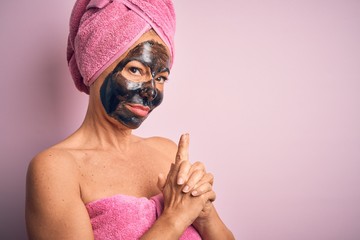 Middle age brunette woman wearing beauty black face mask over isolated pink background Holding symbolic gun with hand gesture, playing killing shooting weapons, angry face