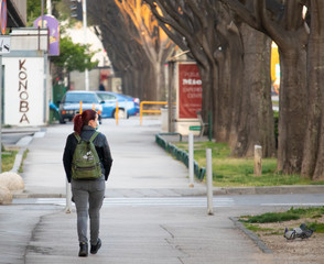 Red headed girl as seen from behind walking on the street wearing a face mask during the coronavirus outbreak pandemic